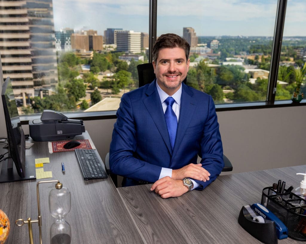 Sean McCrary - Founder - The McCrary Law Firm and I am Injured Colorado smiling at the camera and sitting at desk.
