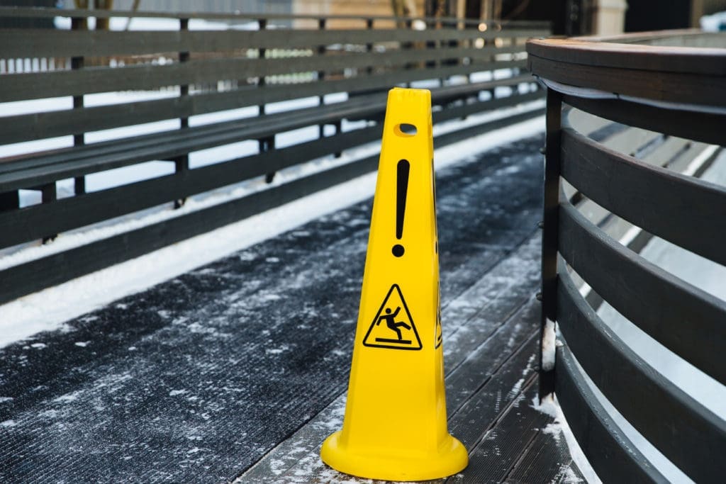 Caution sign warning of slippery floor with a man in the process of falling in the background, emphasizing the importance of understanding slip and fall rights in Colorado.